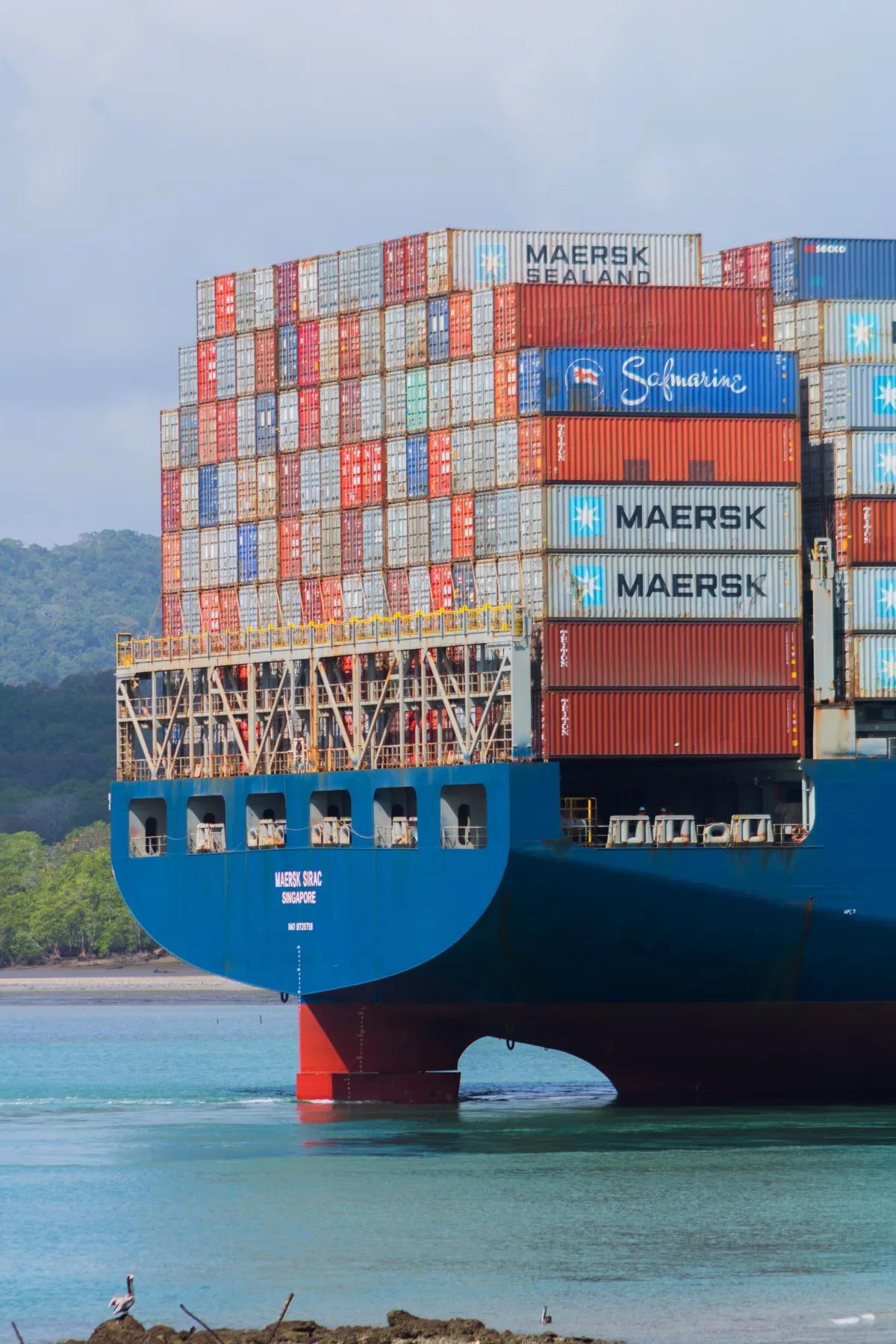 A Maersk container ship stacked high with cargo, viewed from the water